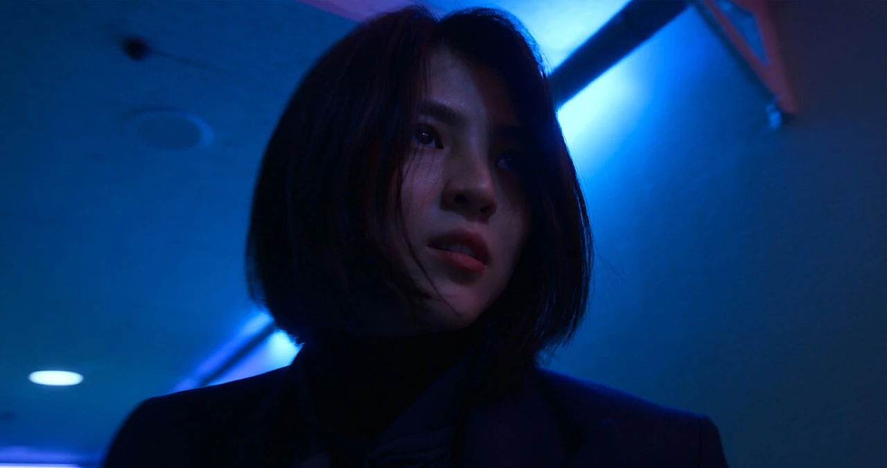 A scene from The Art of Sarah showing one of Sarah Kim's multiple identities in a moody, blue-lit interior