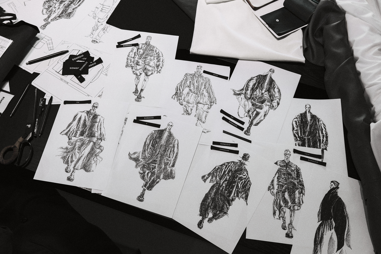 SONGZIO design sketches for BTS Lyrical Armor on atelier table with fabric swatches