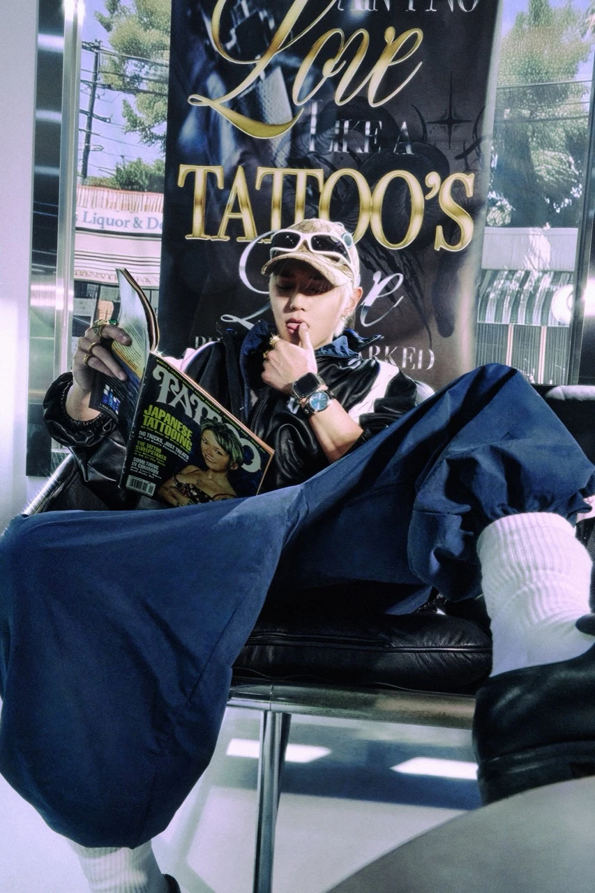 Taeyong seated in a tattoo studio while reading a tattoo magazine in teaser imagery for Rock Solid