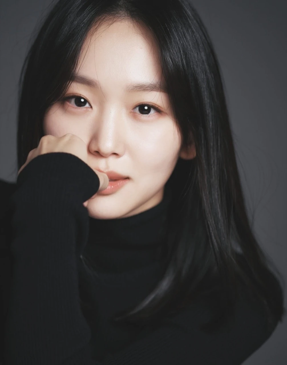 Studio portrait of Jin Ki Joo in a black turtleneck posing with one hand near her face