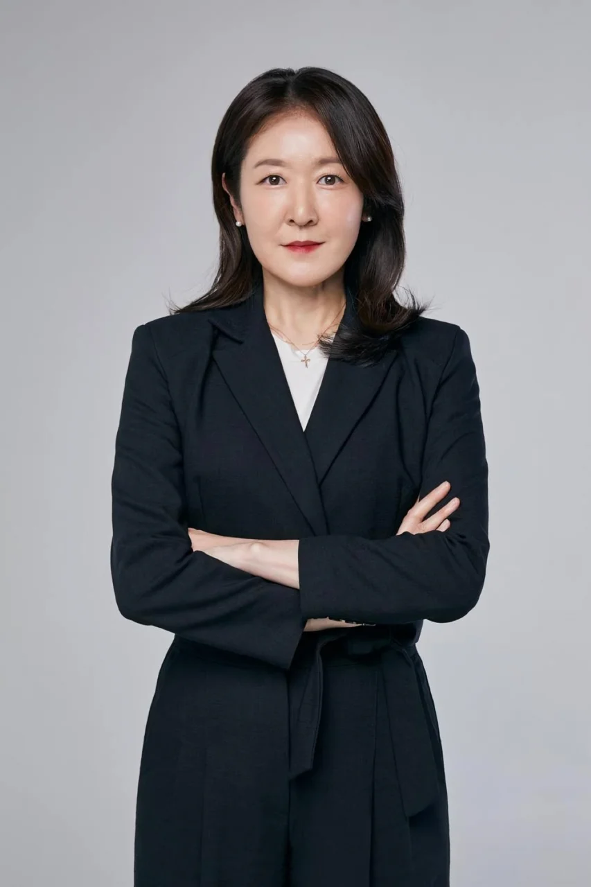 SM Entertainment executive Kim Ji-won in a black suit against a gray studio backdrop