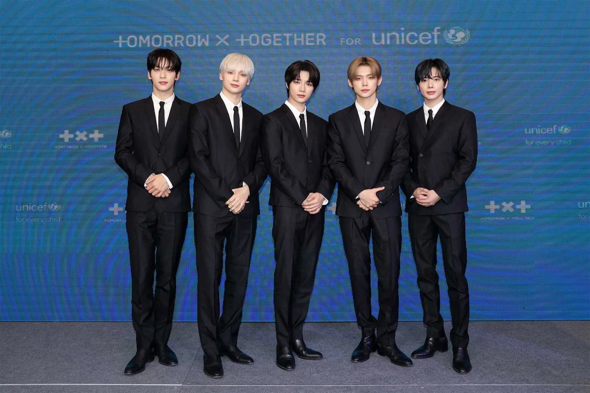 TOMORROW X TOGETHER posing in black suits in front of a Together for Tomorrow UNICEF backdrop