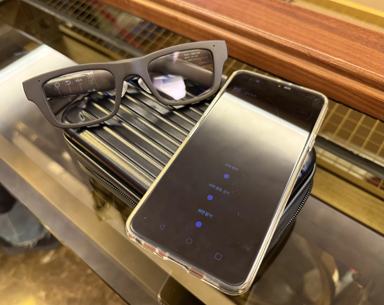 XpertINC Owl subtitle glasses and a smartphone showing Korean subtitle controls on a theater surface