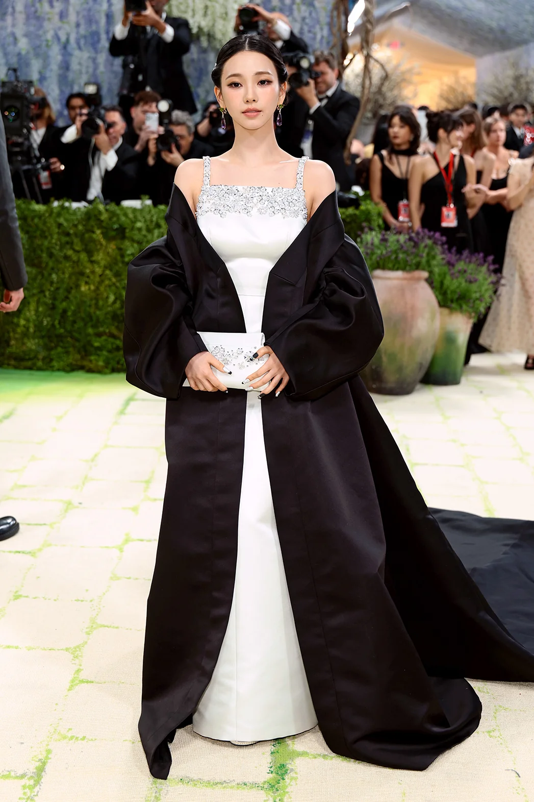 Karina poses on the 2026 Met Gala carpet in a white Prada gown with a dramatic black cape.