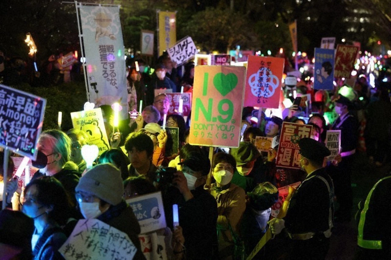 Protesters carry anti-war placards and glowing penlights during a nighttime demonstration in Tokyo