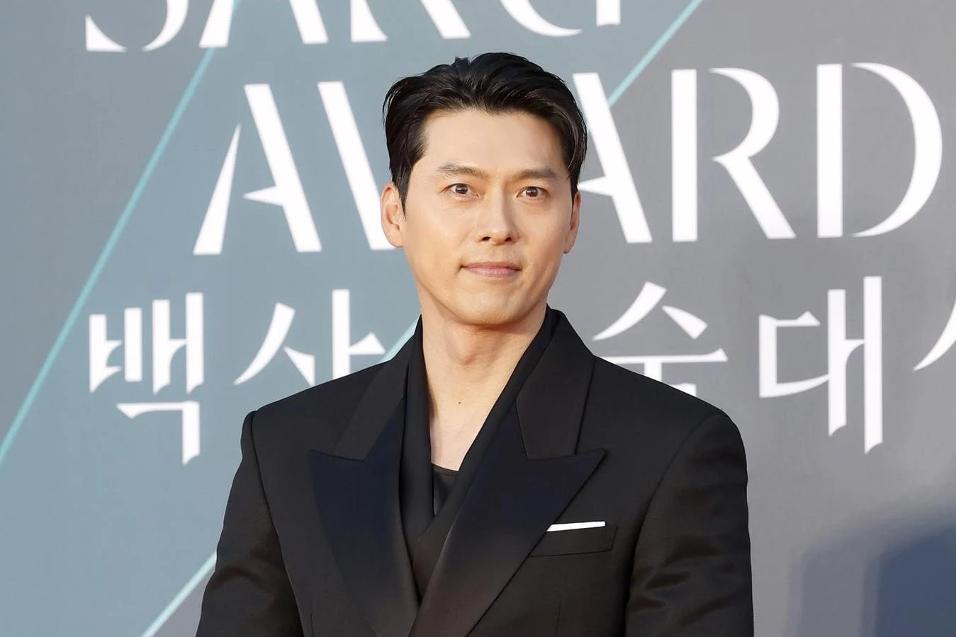 Hyun Bin poses on the Baeksang Arts Awards red carpet in a black tuxedo-style look