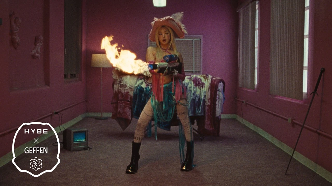 Official promotional still from KATSEYE's PINKY UP era showing a solo performer in a pink room with a burst of flame